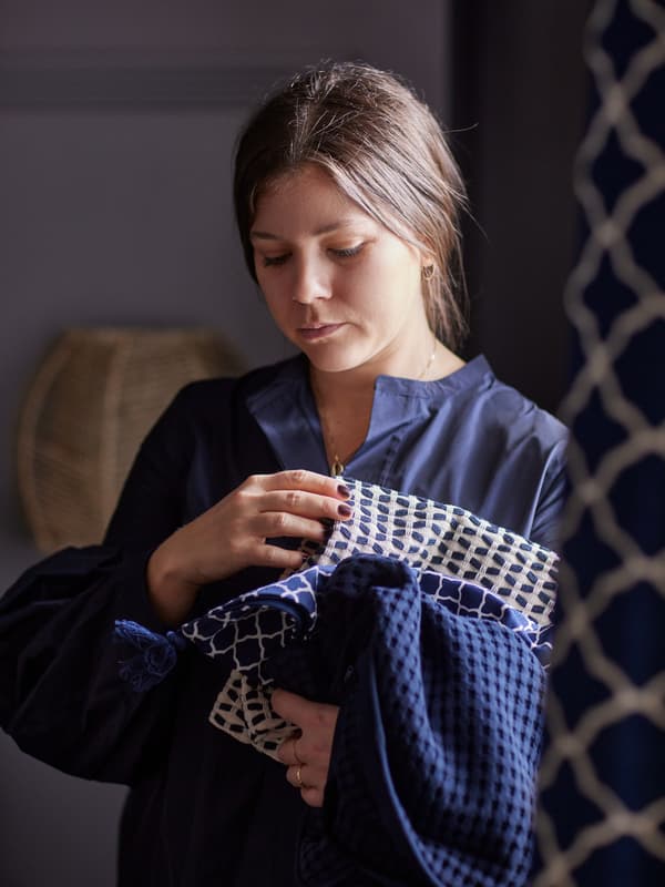 A woman holding folded bedroom textiles in different blue tones and patterns in her arms.