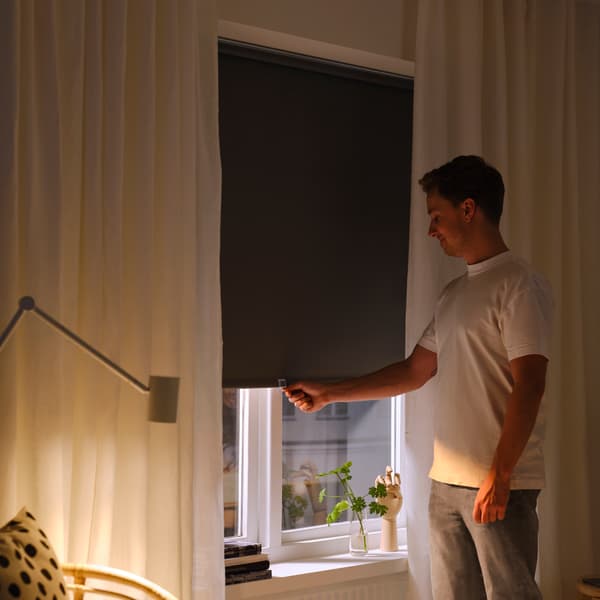 A woman holds red curtains and looks out as the sunlight comes in through the window.