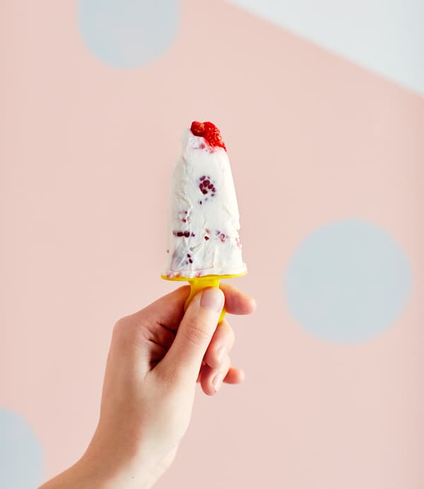 A woman holds up a raspberry frozen yogurt pop.
