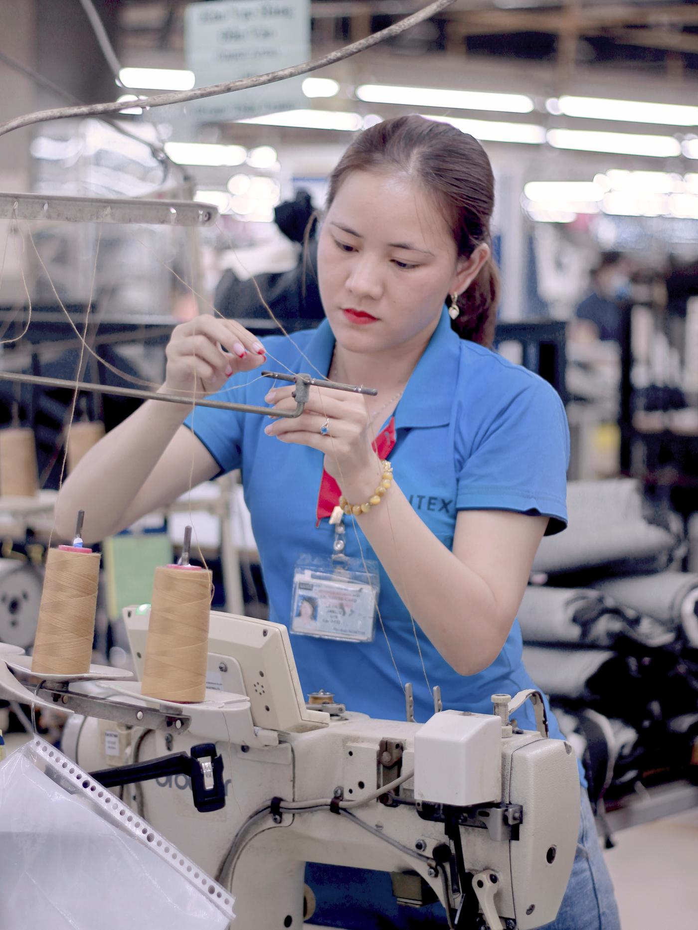 A woman in a blue shirt threads a sewing machine at a Saitex factory in Vietnam.