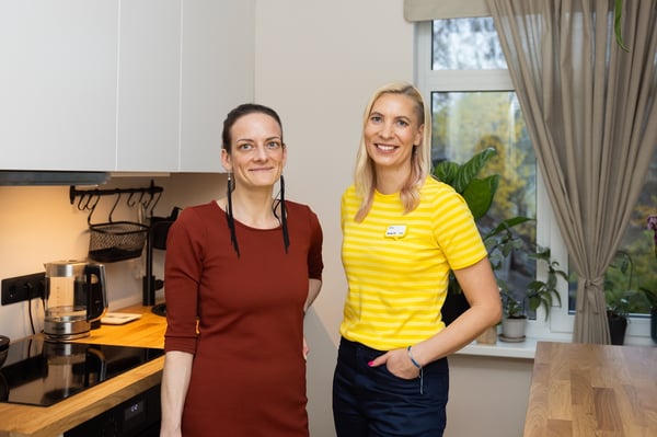 A woman in a red dress and an IKEA interior designer in a yellow uniform in a kitchen with white fronts and a wooden worktop.