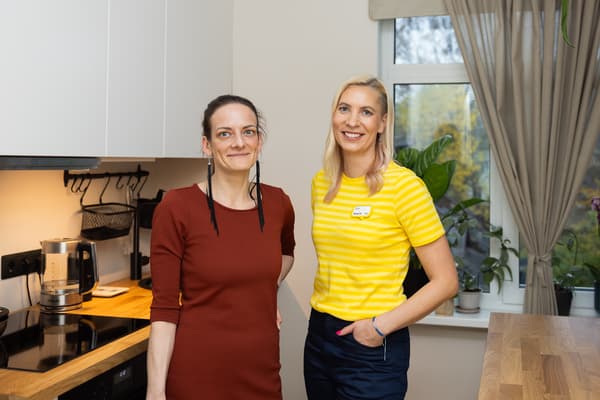 A woman in a red dress and an IKEA interior designer in a yellow uniform in a kitchen with white fronts and a wooden worktop.