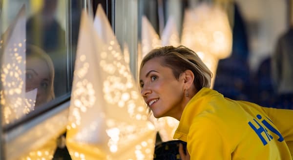 A woman in an IKEA uniform looks out the window in delighted surprise alongside a whole row of STRÅLA stars hanging on the wall.