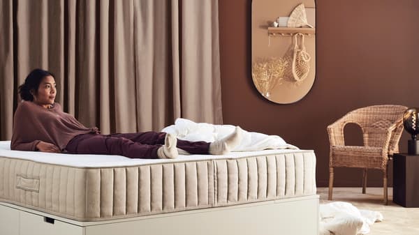 A woman in comfortable clothes lies on the mattress with her arms behind her body.