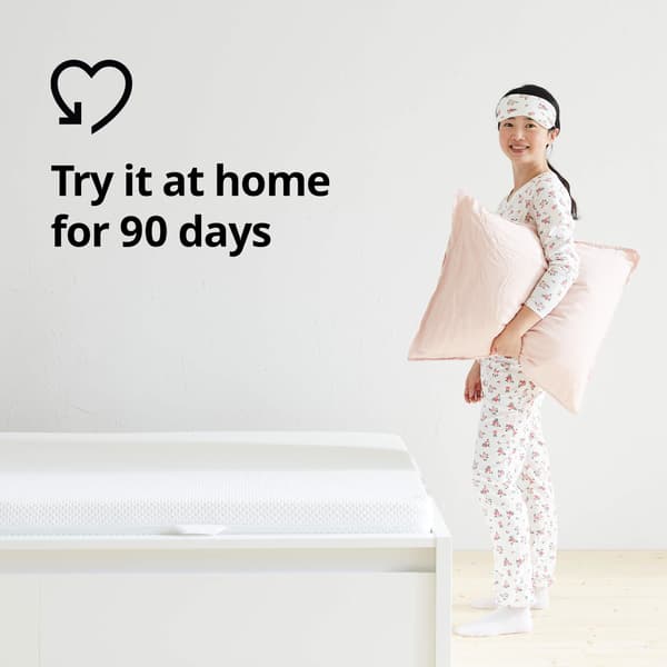 A woman in her pajamas holding a pillow next to a bed and a heart graphic and the text 'Try it at home for 90 days' on the image.