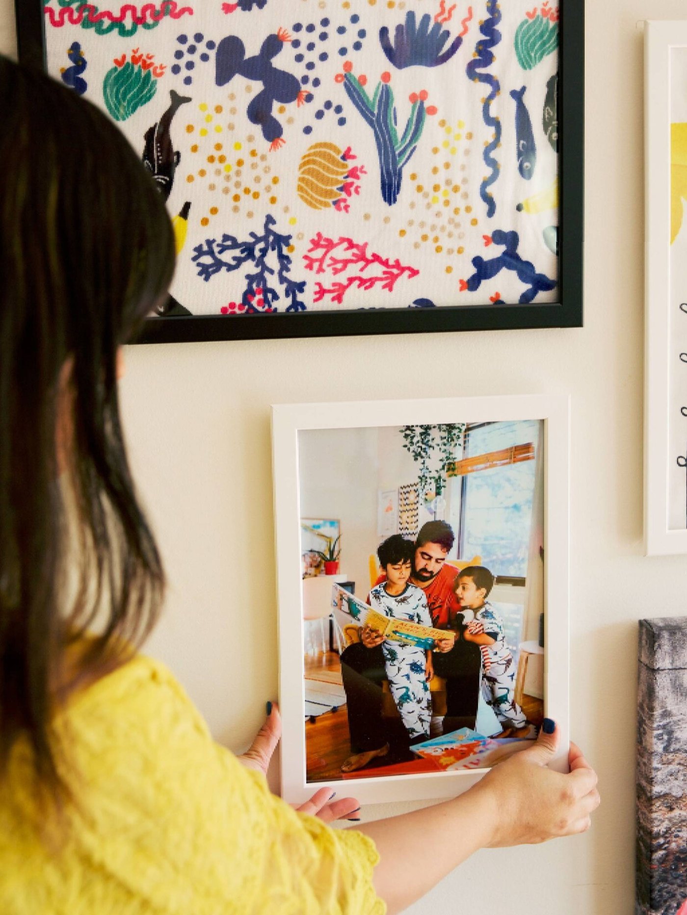 A woman in yellow positioning a family photo on a gallery wall of pictures.