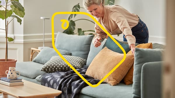 A woman is fluffing some pillows on a blue sofa.