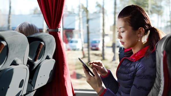 A woman is sitting inside a bus, holding her phone with her one hand, and tapping on it with the other.