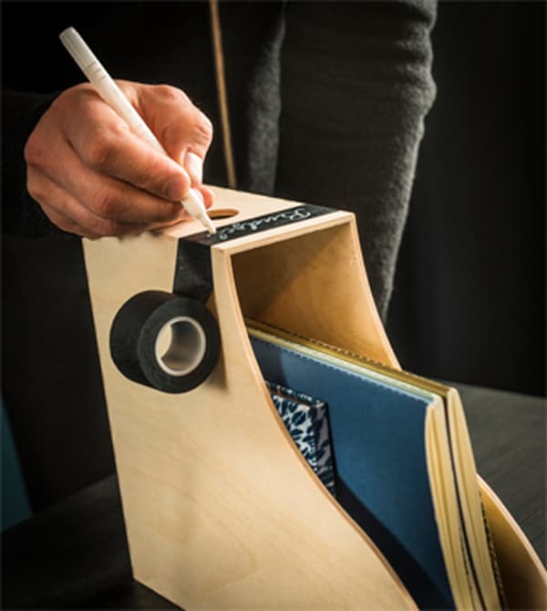 A woman labels the front of a magazine file with a black roll of tape.