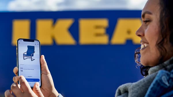 A woman looking at the IKEA app on her mobile device while standing in front of an IKEA store.