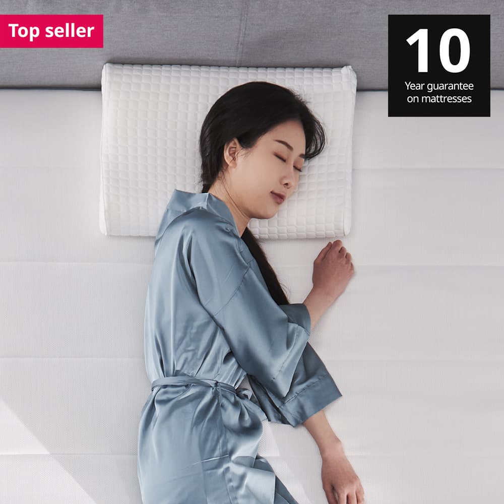 A woman lying on KLUBBSPORRE pillow on a latex extra firm/light blue VITMÅSEN pocket sprung mattress. 10 year guarantee on IKEA mattresses.