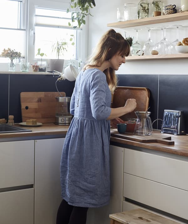 A woman making tea in the corner of a blue and white kitchen.