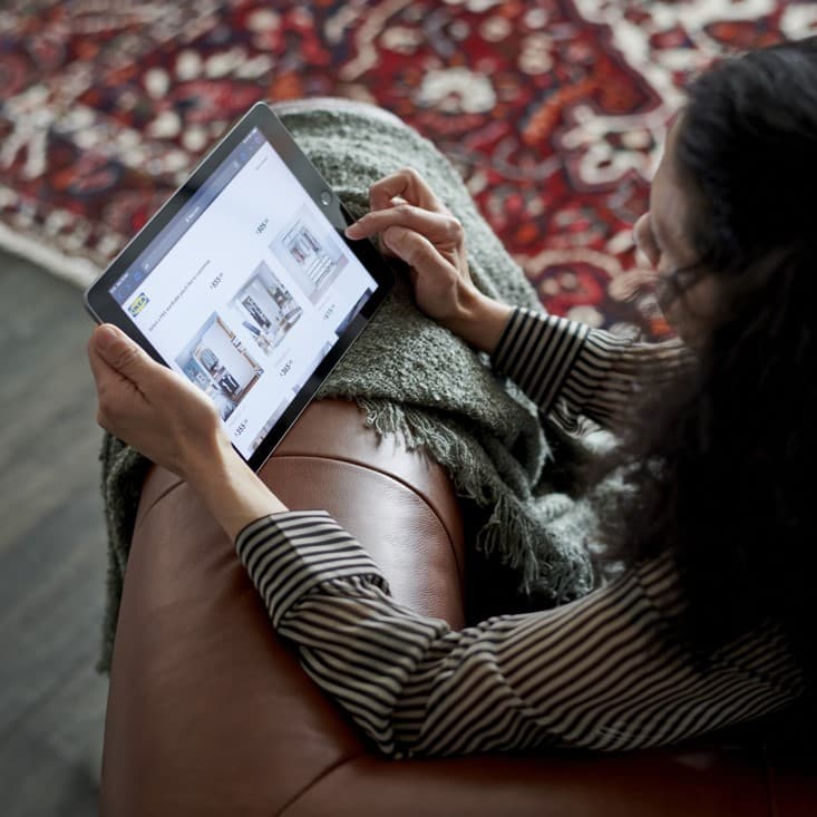 A woman on a brown leather sofa designing a room on her tablet.