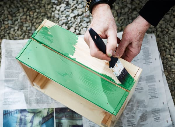 A woman paints a wooden planting box green.