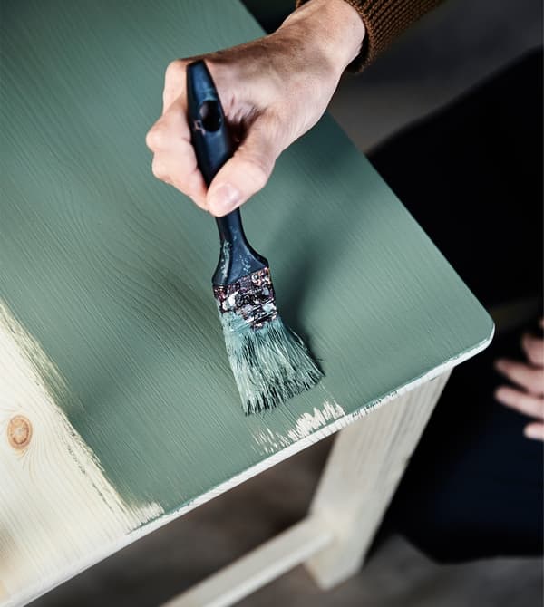 A woman paints an old chair in a new green colour.