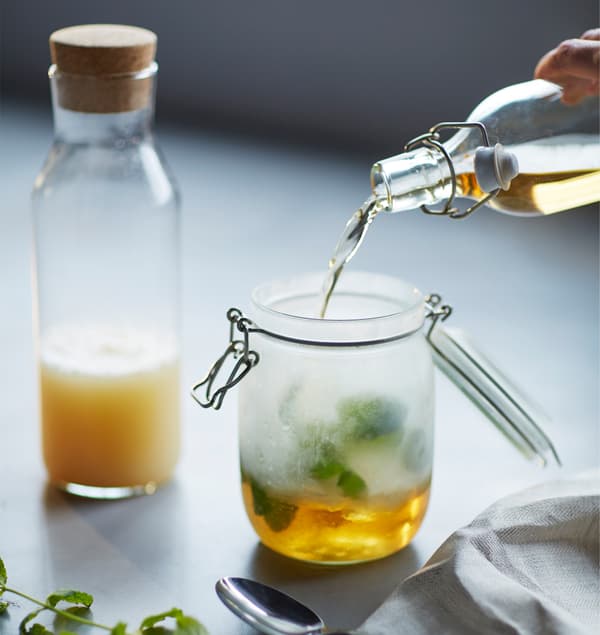 A woman pours ginger beer into a jar.