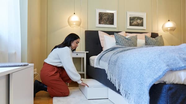 A woman pushes a bed box under a bed