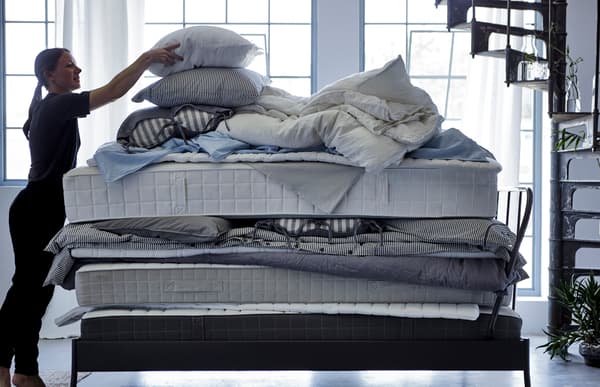A woman putting a pillow on top of a stack of soft mattresses, quilts and bed textiles. 