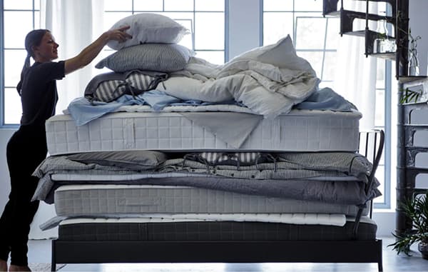 A woman putting a pillow on top of a stack of soft mattresses, quilts and bed textiles