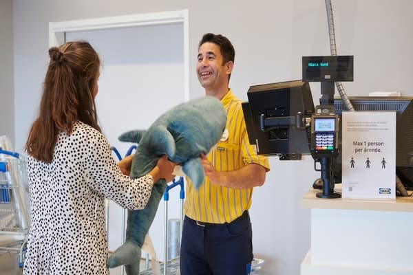 A woman returning a large soft toy shark to a co-worker in an IKEA uniform at an IKEA store.