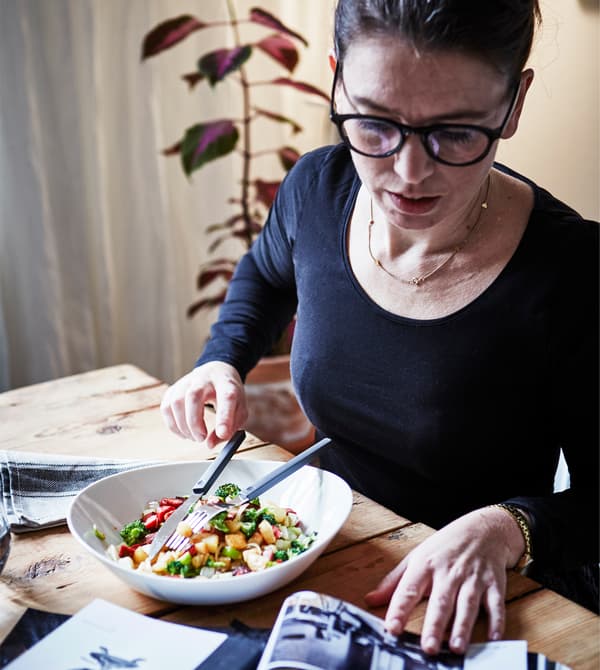 A woman sits at a table with a bowl of food and a magazine