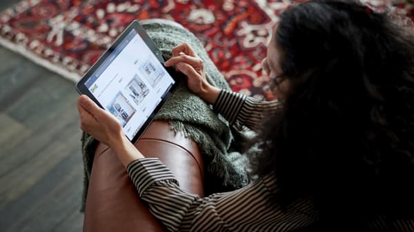 A woman sits on the sofa with a tablet and browses the IKEA website.