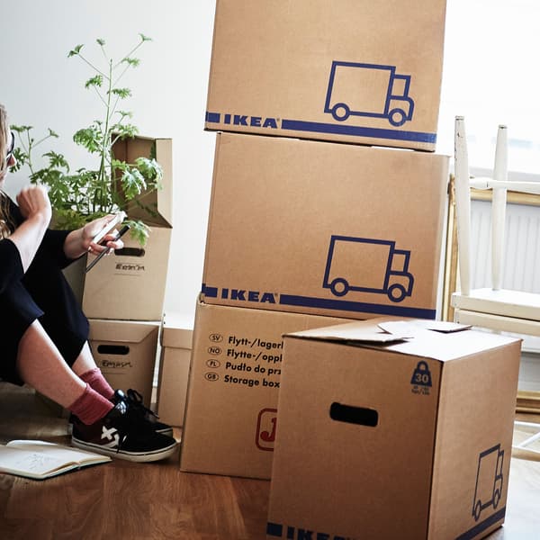 A woman sitting on a wooden floor surrounded by JÄTTENE cardboard boxes.