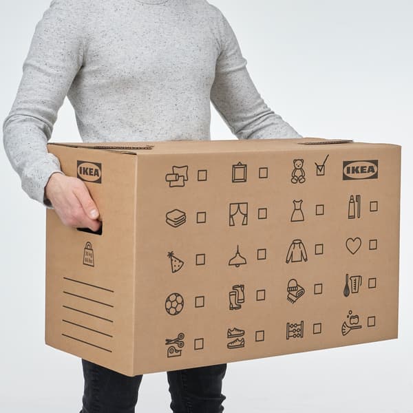 A woman sitting on a wooden floor surrounded by various boxes including a pile of JÄTTENE boxes.