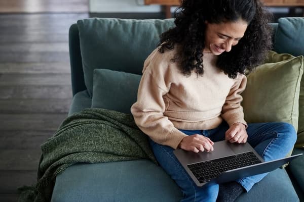 A woman sitting on her sofa at home with a laptop on her knees.