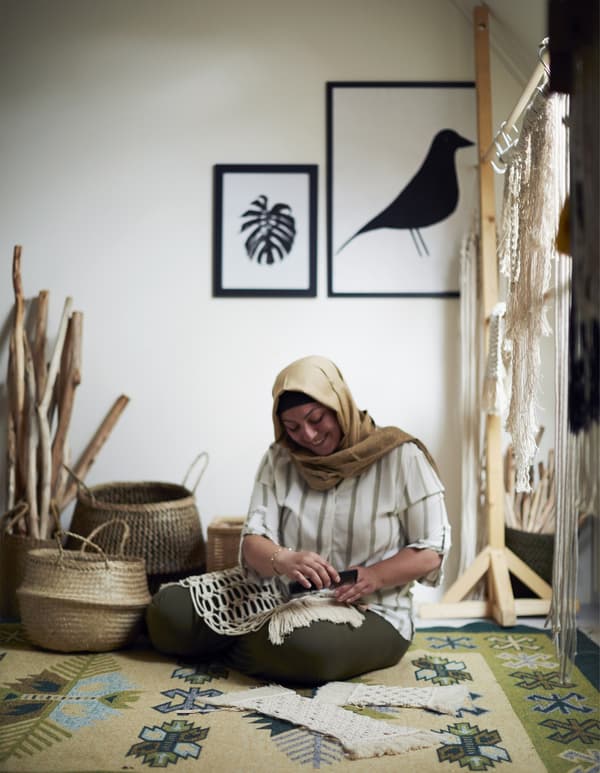 A woman sitting on the floor making macramé creations.