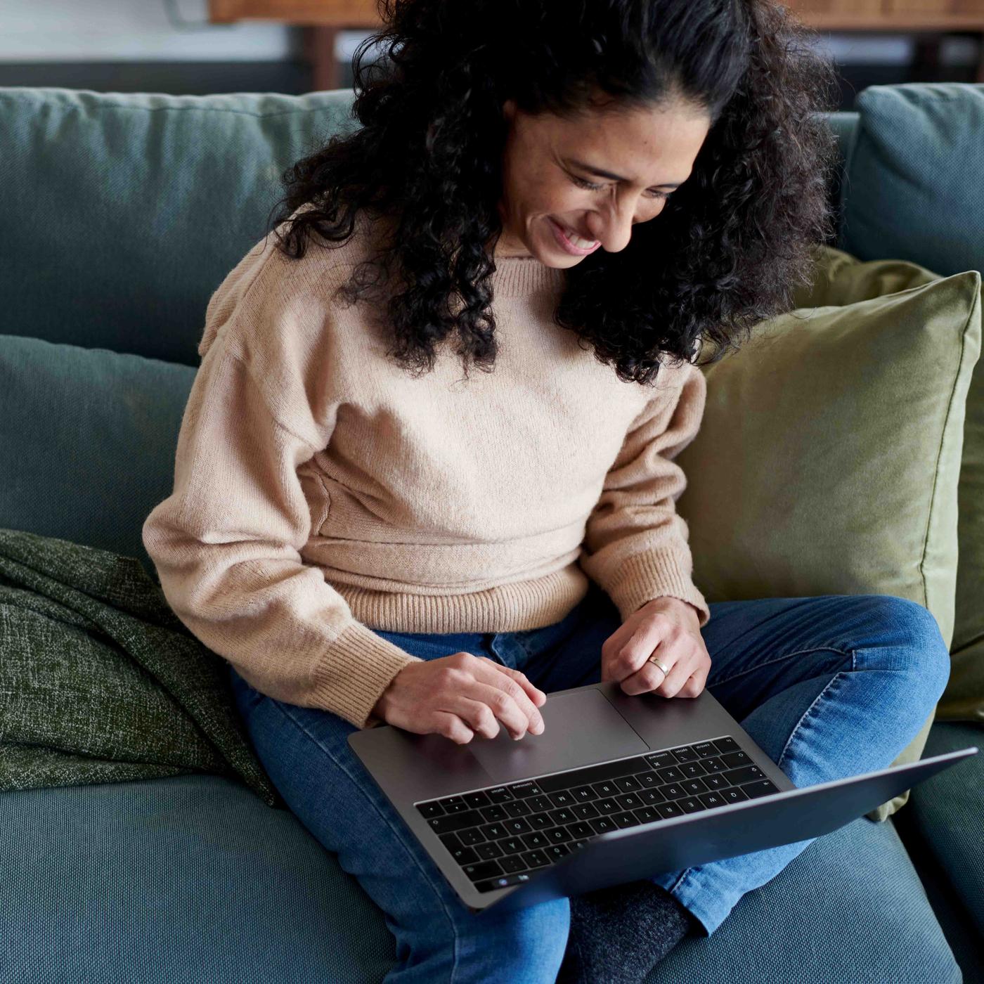 A woman sitting on the sofa with a laptop on her lap.