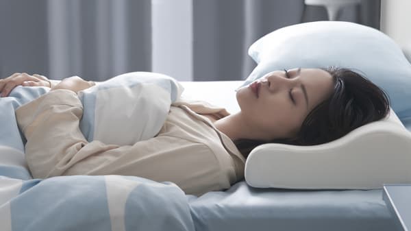 A woman sleeping on her back with her head resting on a KLUBBSPORRE ergonomic pillow.