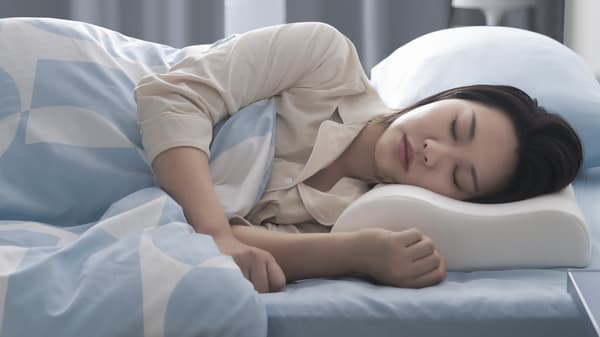 A woman sleeping on her side with her head resting on a KLUBBSPORRE ergonomic pillow.