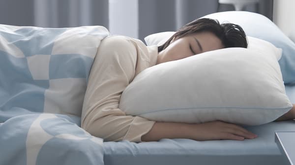 A woman sleeping on her stomach with her head resting on a big fluffy pillow.