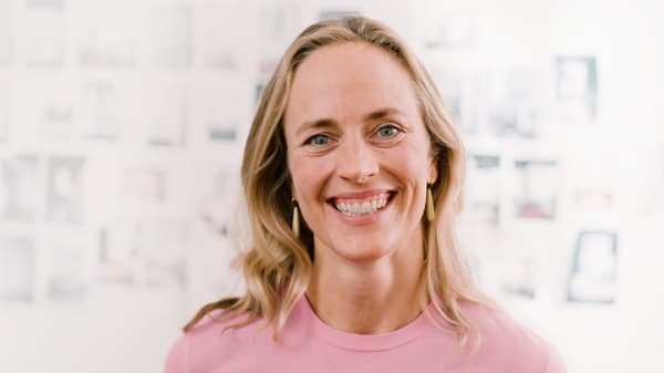 A woman smiling at the camera with a white patterned wall background.