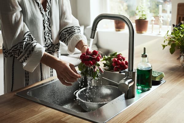 A woman standing by the sink rinsing radishes using the ÄLMAREN kitchen tap.