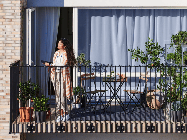 A woman stands on her balcony with a tablet in her hand