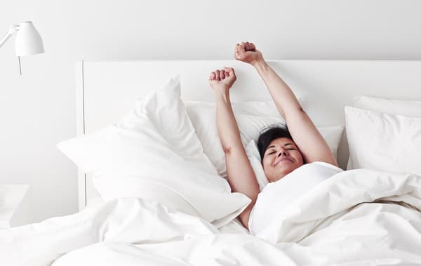 A woman stretching in bed after a good night's sleep.