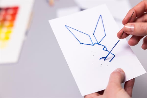 A woman threads a needle and sews a rabbit out of a piece of paper.