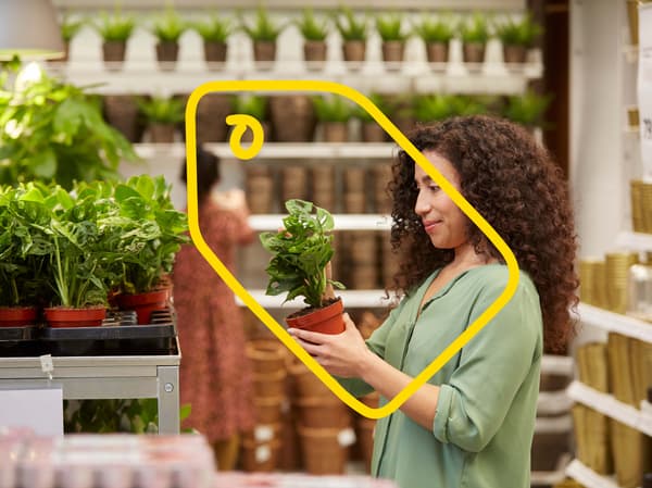 A woman wearing a green tshirt and holding a plant in an IKEA store.