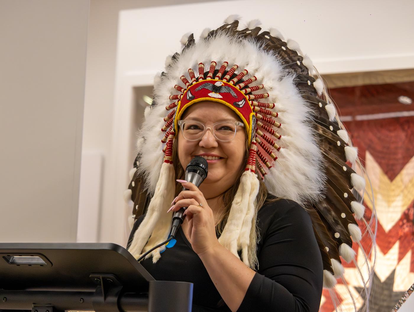 A woman wearing a headdress holds a microphone at a podium.
