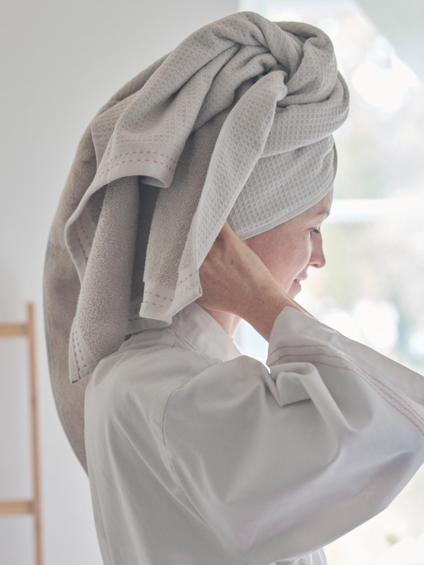 A woman wearing a VÅRDANDE cotton kimono uses a VÅRDANDE towel as a turban to dry her hair.