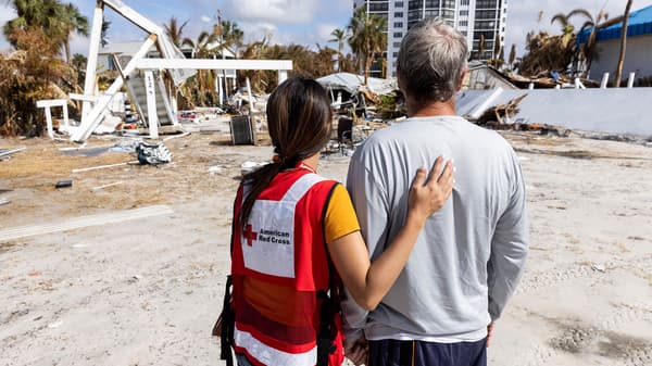A woman wearing an American Red Cross vest with her hand on the back of a man.