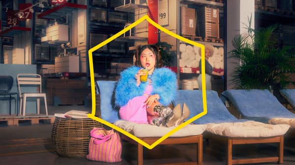 A woman wearing colourful clothes eats a lollipop and sits on a sun bed in an IKEA store. 