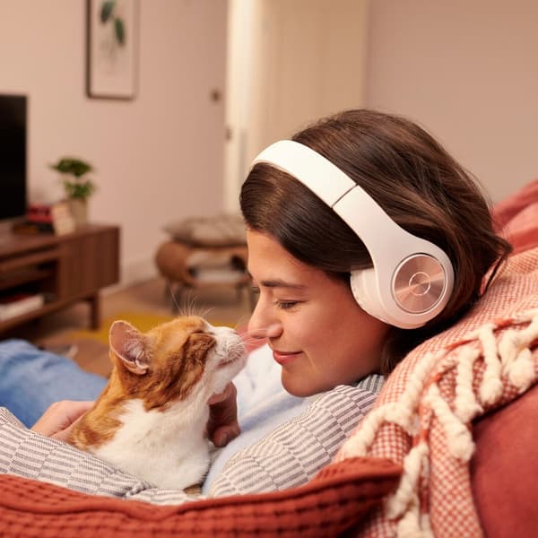 A woman wearing headphones is sitting on a sofa and stroking a cat on her lap.