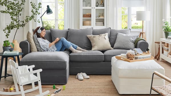 A woman wearing headphones relaxes on a GRÖNLID three-seat sofa with chaise lounge in a family living room.