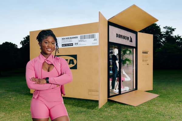 A woman wearing pink gym wear in front of a life-size IKEA flatpack box containing a store called DamiHow.