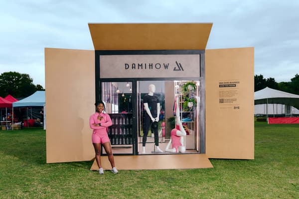 A woman wearing pink gym wear in front of a life-size IKEA flatpack box containing a store called DamiHow.