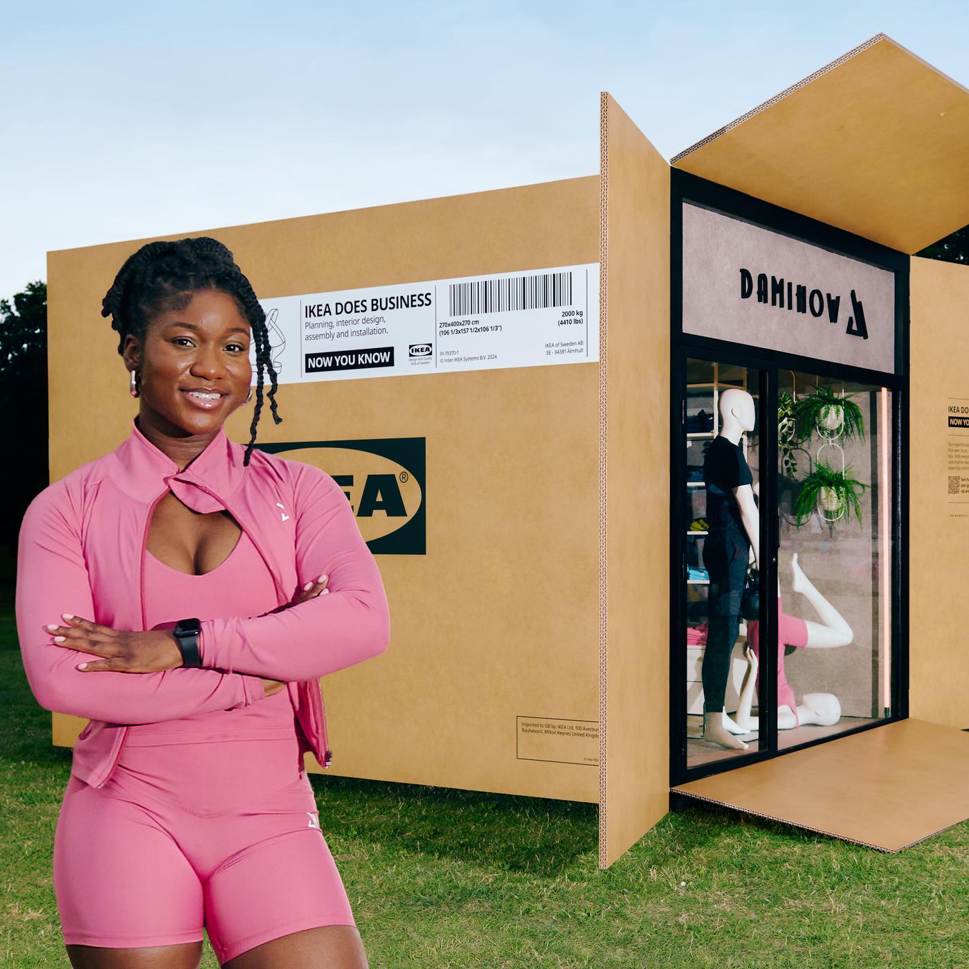 A woman wearing pink gym wear in front of a life-size IKEA flatpack box containing a store called DamiHow.
