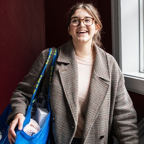 A woman with a blue IKEA bag on her shoulder is smiling as she walks up some steps.
